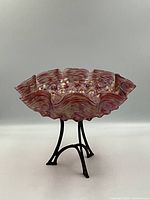 Front side view of antique Bohemian art glass bowl mounted on a black metal tripod stand against white background.