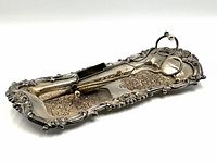 Side view of silverplate tray with ornate floral and scalloped edge design, holding the snuffer scissors.