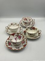 Four bone china teacups with matching saucers arranged showing floral and gilt details.