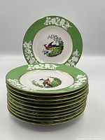 Stack of 11 green-bordered plates showing central peacock motif and gilt rims