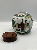 View of ginger jar with wooden piece to the side showing hand painted figures and detail
