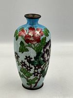 Front view of hand-enameled bud vase with floral pattern and light blue background.