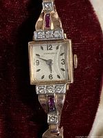 Front view of watch face and lugs inside velvet box, showing square dial, diamond and ruby accents