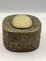 Front view of oval brass box with white jade center and turquoise insets