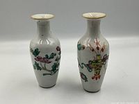 Pair of Asian antique bud vases standing side by side showing differing painted designs