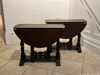 Photo showing both drop-leaf oak side tables facing front with leaves folded down. Highlights turned legs and stretcher base.