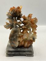 Front view of soapstone carving showing bird and flower details mounted on a thick rectangular pedestal.