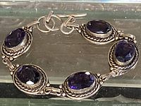 Full view of bracelet laid flat showing five oval amethyst links and toggle clasp