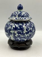 Front view of the covered jar on the wooden stand showing intricate blue and white floral patterns.