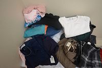 Pile of assorted folded clothing including pants, shorts, and shirts in various colors and patterns.