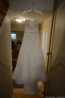 Front view of the white strapless wedding dress hanging, showing the sequined bodice and full skirt with train.