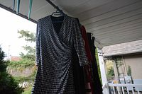 Black and white houndstooth patterned wrap dress with ruched detail, visible with multiple other dresses hanging on rack outdoors