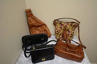 Five vintage handbags arranged on a surface, showing variety of styles and colors including brown leather backpacks, black embossed leather handbag, and floral fabric handbag with tassel