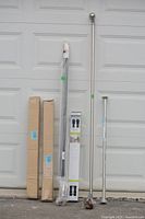 Set of curtain rods, blinds, and shower rods displayed against a garage door, showing overall lot contents and packaging.