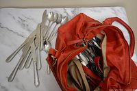 Photo showing a selection of knives and spoons alongside a red bag containing further cutlery items.
