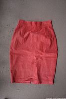 Front view of a pink suede skirt, pencil style with pleats and back slit.