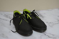 Pair of black leather Doc Martens shoes with lace-up front and side zipper, showing overall design and condition on marble surface.