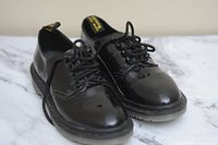 Pair of black patent leather Doc Martens shoes showing glossy finish and black laces.