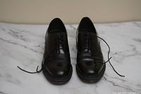 Front view of the pair of black leather lace-up Doc Martens shoes on a white marble surface.