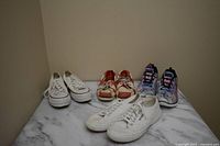Four pairs of shoes displayed on marble surface: white Vans Converse, red and white Dockers Sebago Dockside, multicolor Skechers, white Superga shoes.