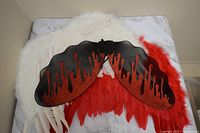Devil wings with black and red glitter in a dripping blood pattern, red feather trim, and attached straps laid flat.