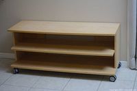 Photo of the Ikea BENNO TV unit showing three open shelves, birch wood veneer finish, and lockable caster wheels.