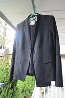 Black Ann Taylor women's suit jacket and pants hanging on a hanger outdoors.