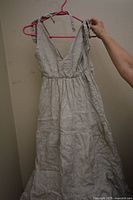 Sleeveless linen dress with shoulder ties and gathered waist hung on a pink hanger