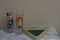 Eight clear glasses with colorful billiard ball designs beside ceramic triangle chip bowl