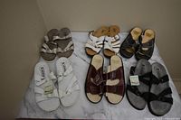 Top view of six pairs of women's summer sandals in various colors and styles on a marble background.