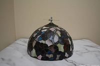 Side view of the dome-shaped Tiffany style stained glass lampshade showing colorful floral pattern in dark purple, blue, pink, cream, and red glass pieces with black outlines.