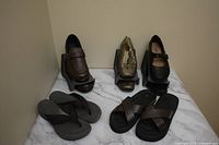 Photo of various men's and women's shoes including loafers, heeled shoes, mule slippers, and sandals arranged on a marble surface against a beige wall.