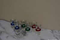 Six vintage 1950s shot glasses arranged in a row on a marble surface, showing blue, green, and red bands.