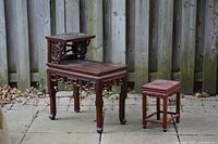 Photo showing the full set of two solid wood tables on outdoor pavement in front of wooden fence.
