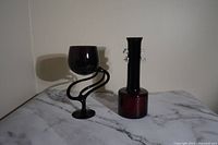 Two deep aubergine vintage flower and vase holders on a marble surface against a plain wall