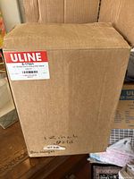 Closed cardboard box labeled Uline containing 12 inch gold scalloped pads, quantity 100.