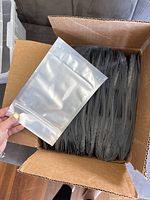 Box filled with many medium plastic resealable bags. One bag held up showing clear front and silver back with ziplock seal.
