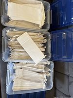 Three clear plastic storage bins filled with stacks of white paper bags for 2 lb coffee; one bag displayed on top of each stack.