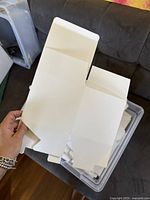 Hand holding a single flat, unfolded white cardstock bakery box showing fold creases and tabs.