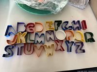 Full set of 52 alphabet cookie cutters displayed in rows on a white surface. Multiple colors and repeated letters are visible.
