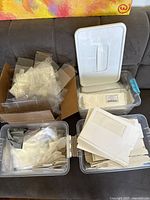 Boxes and packaging materials including stacks of white cardboard candy boxes with windows and multiple plastic containers filled with clear cello bags and small clear plastic boxes
