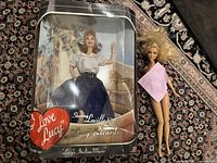 Collector's doll of Lucille Ball in original box with floral background, unopened but box shows minor wear. Next to it a loose blonde Barbie doll.