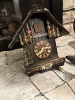 Angled front view highlighting hand-painted floral designs, clock face with Roman numerals, and pine tree side decoration.