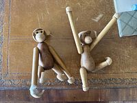 Two wooden monkey figurines on a wooden table, showing both front and side views with visible wear and one taped broken hand.