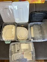 Top view of three open plastic storage boxes showing stacks of paper doilies and clear plastic moulds inside
