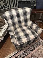 Front view of the wingback armchair showing plaid upholstery in black, white, and grey with rolled arms and cushioned seat.