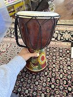 Side view of djembe drum showing wooden body with colorful dot pattern and black rope tuning.