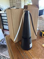 Two black electric fly repellers in cone-shaped design, placed on a wooden surface beside their cardboard boxes.