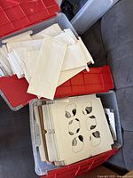 White paper bags and cardboard inserts stored in clear plastic bins with red lids. Bags are plain and stacked in one bin, cardboard inserts with cutouts for cups are stacked in another bin.