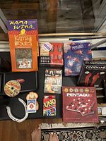Photo showing a collection of games, DVDs, and books on a table with boxes and cases of various board and card games, DVDs and books including Kama Sutra and Perry Mason series.